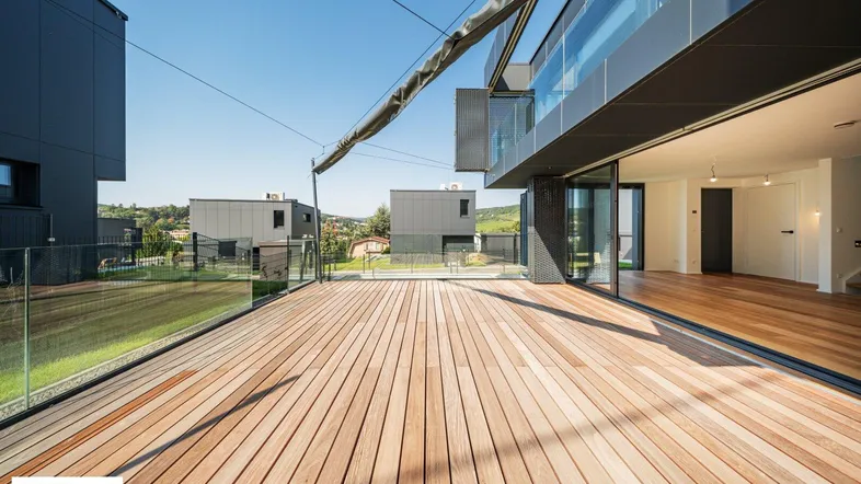 Große Holzterrasse mit Glasgeländer und Blick auf die umliegende Landschaft, direkt vom Wohnbereich zugänglich.