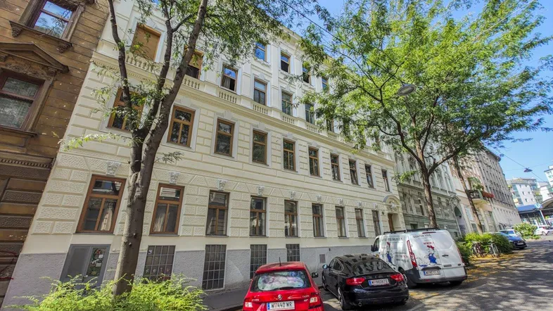 Gepflegte Altbaufassade mit klassischer Architektur und Bäumen entlang der Straße.