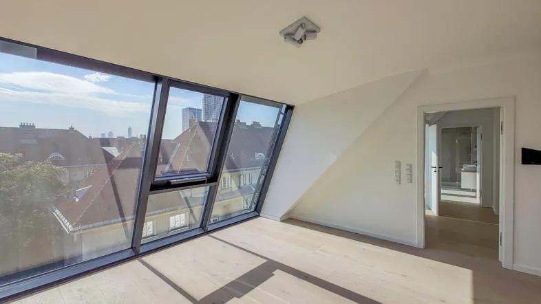 Heller Raum im Dachgeschoss mit großen Schrägfenstern, Holzboden und Weitblick über die Stadt.
