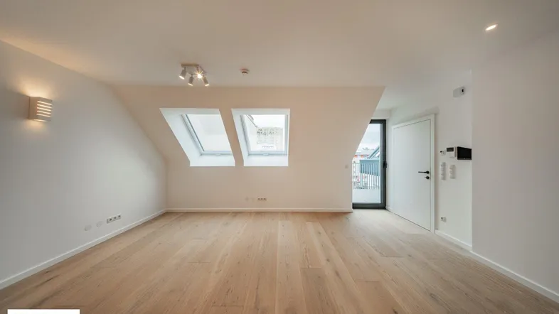 Heller Wohnraum im Dachgeschoss mit Holzboden, Dachfenstern und Zugang zu einem Außenbereich.