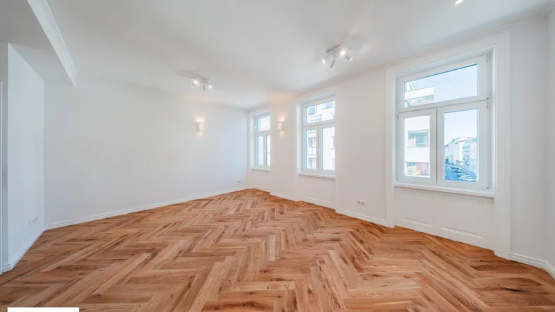 Helles Zimmer mit Fischgrätparkettboden und mehreren Fenstern, ideal für Wohn- oder Schlafbereich.
