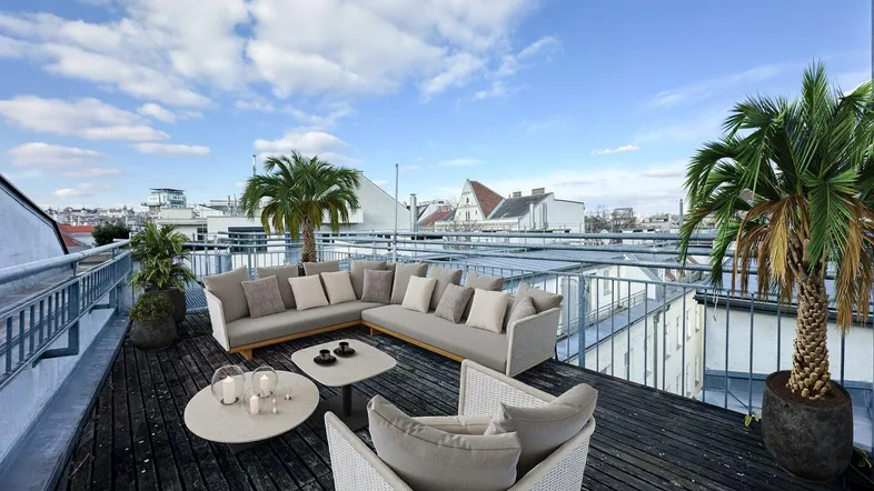 Geräumige Dachterrasse mit bequemen Loungemöbeln, Palmen und weitem Blick über die Stadt.