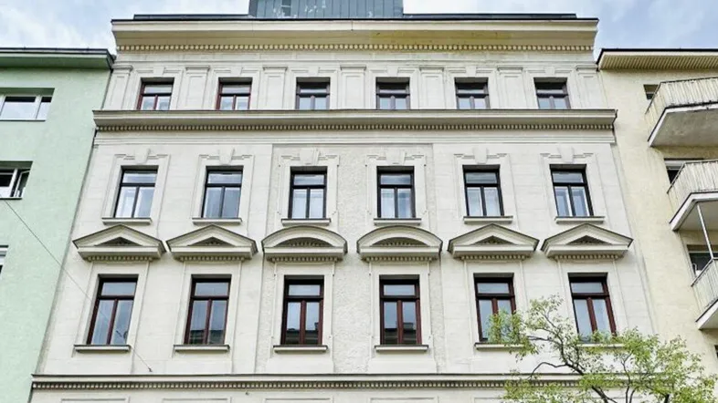 Historisches Gebäude mit klassischer Fassade und modernem Dachausbau in städtischer Umgebung.