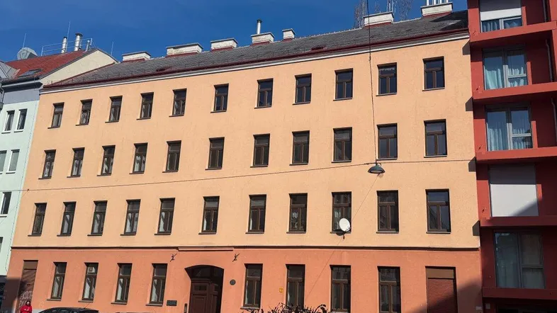 Historisches Wohngebäude mit orangefarbener Fassade und traditionellen Fenstern unter blauem Himmel.