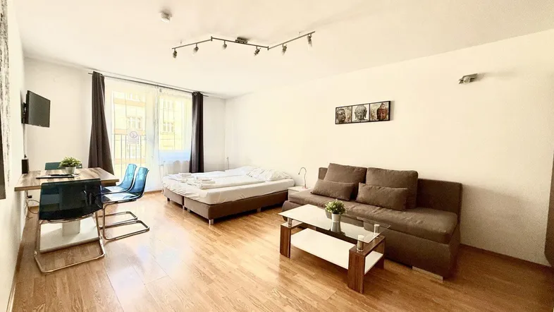 Helles Wohnzimmer mit Holzboden, Schlafbereich, Sofa und Esstisch, ideal für ein Studio-Apartment.