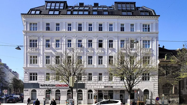 Klassisches Altbaugebäude mit modernisiertem Dachgeschoss und Geschäften im Erdgeschoss an einer belebten Straße.