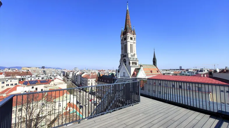 Geräumige Dachterrasse mit Holzboden und weitem Blick über die Stadt und eine historische Kirche.