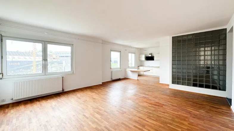 Geräumiger Wohn-Essbereich mit Parkettboden, großen Fenstern und integrierter Küche.