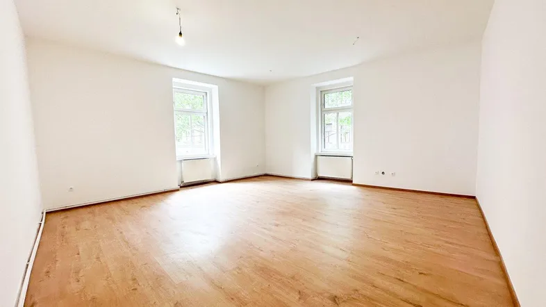 Heller, leerer Raum mit Holzfußboden und zwei Fenstern, bereit zur individuellen Gestaltung.