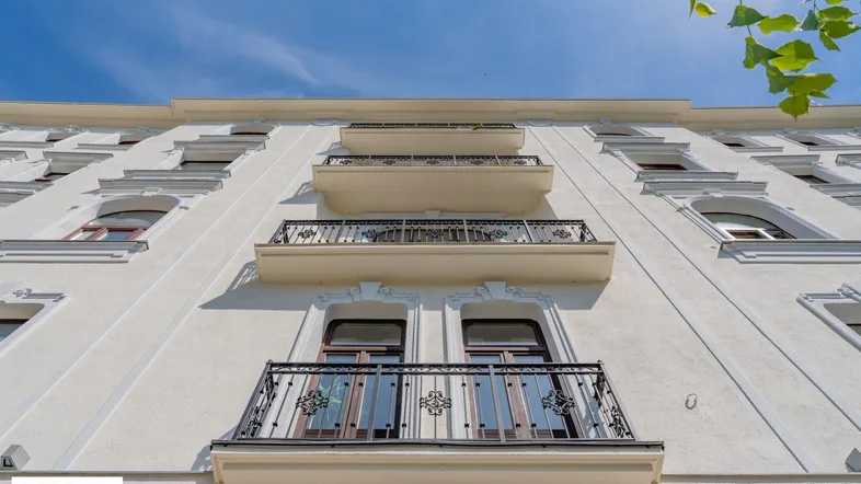 Fassade eines Gebäudes mit mehreren kleinen Balkonen und dekorativen Geländern unter blauem Himmel.