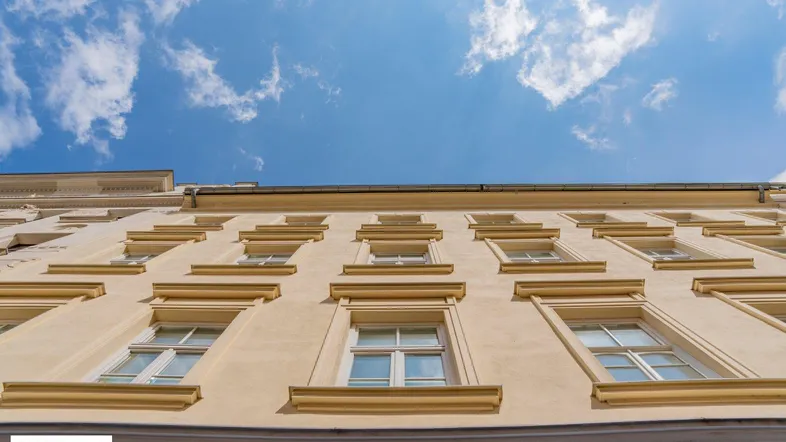 Blick nach oben auf die Fassade eines Altbaus mit vielen Fenstern unter einem blauen Himmel mit Wolken.