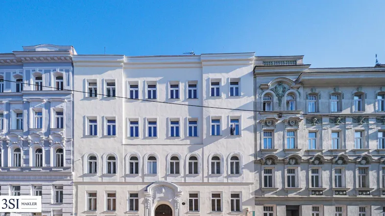 Historische Gebäudezeile in einer Stadtansicht mit einer weiß gestrichenen Fassade in der Mitte.