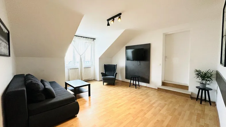 Helles Wohnzimmer mit Dachschrägen, Holzboden und gemütlicher Einrichtung im Dachgeschoss.