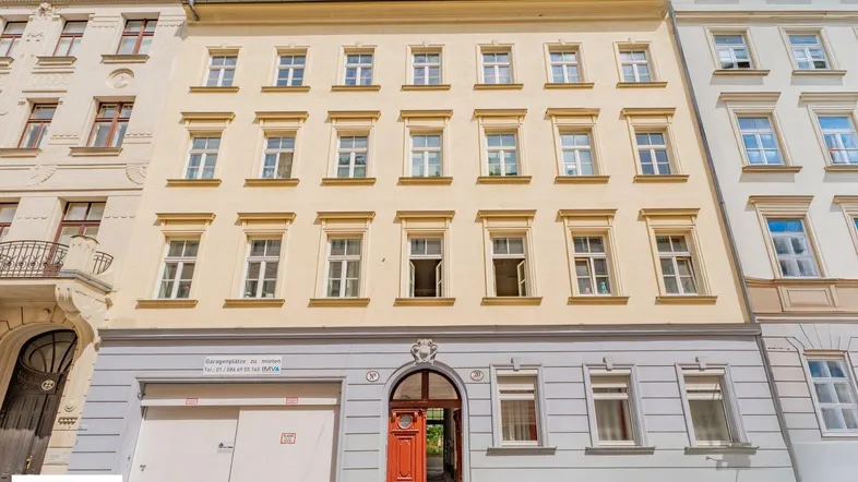 Historisches Mehrfamilienhaus mit gelber Fassade, vielen Fenstern und einer Garage im Erdgeschoss.