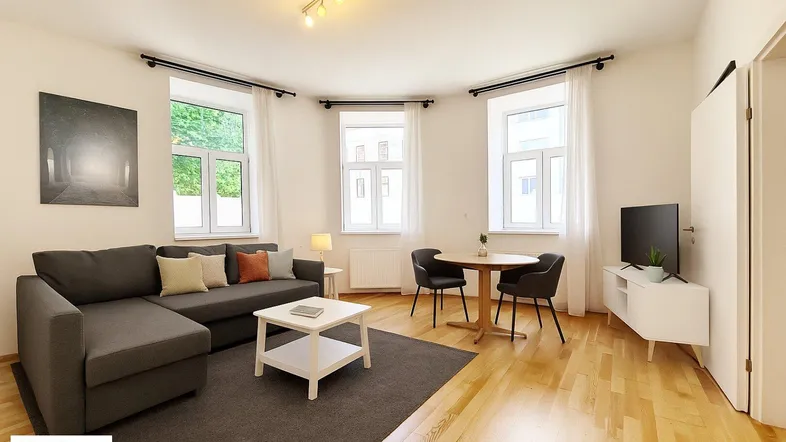 Helles Wohn- und Esszimmer mit modernem Sofa, Holzboden und mehreren Fenstern.