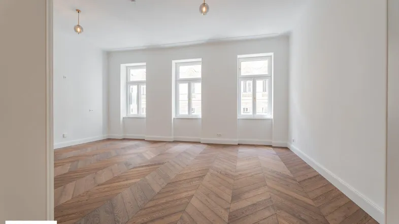 Helles Wohnzimmer mit Fischgrätparkettboden, hohen Decken und großen Fenstern.
