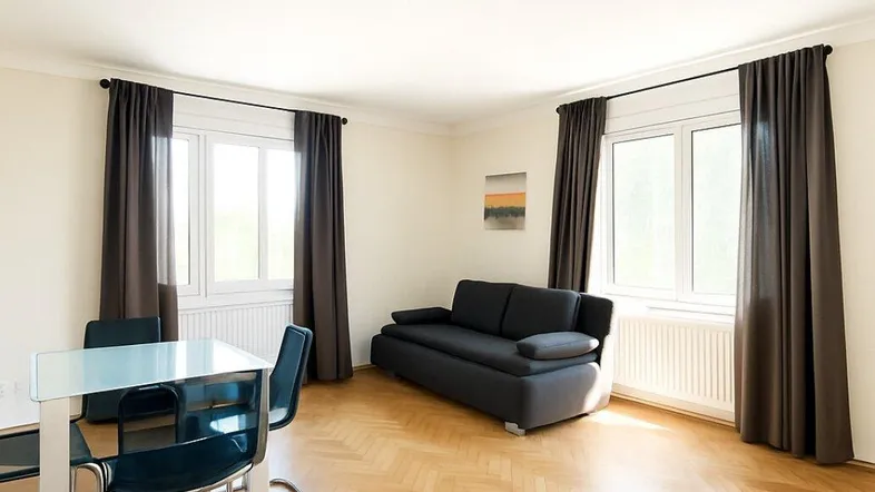 Helles Wohn- und Esszimmer mit Fischgrätparkett, dunklen Vorhängen und einem Sofa.