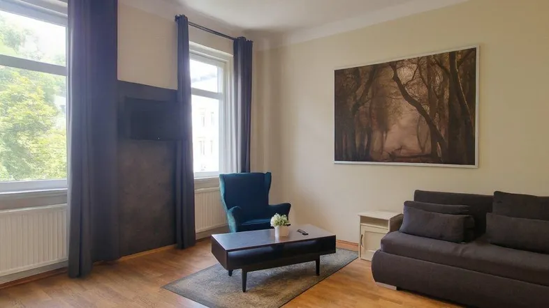Helles Wohnzimmer mit Parkettboden, bequemer Couch und Blick ins Grüne durch große Fenster.