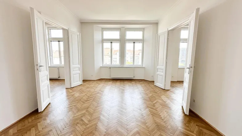 Helles Zimmer mit Fischgrätparkett und hohen Fenstern, das viel Tageslicht hereinlässt.