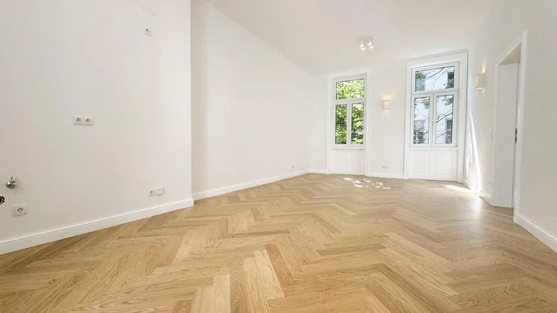 Heller Raum mit elegantem Fischgrätparkett und großen Fenstern, die viel Tageslicht hereinlassen.