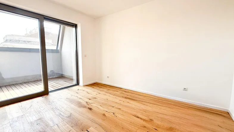 Helles Zimmer mit Holzboden und Zugang zu einem Balkon, ideal als Wohn- oder Schlafbereich.