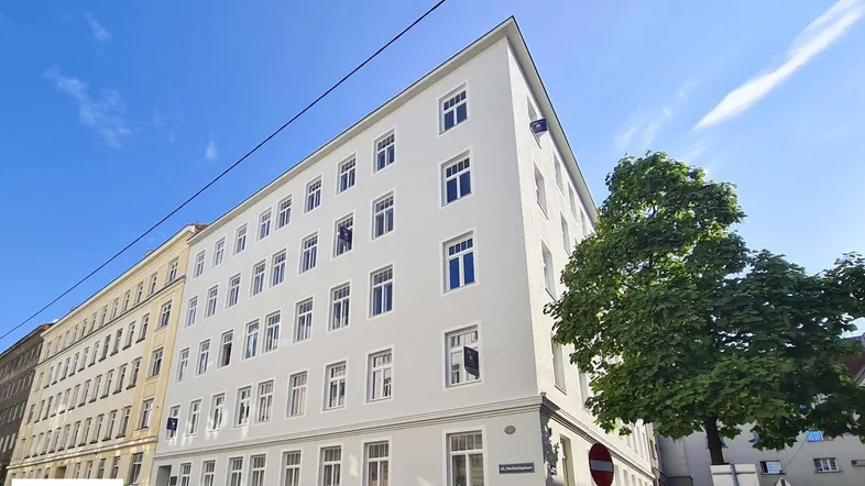 Außenansicht eines Eckgebäudes mit mehreren Stockwerken und klassischer Architektur in städtischer Umgebung.