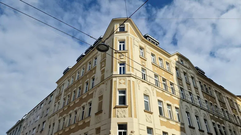 Historisches Eckgebäude mit reich verzierter Fassade unter blauem Himmel und klaren Linien.