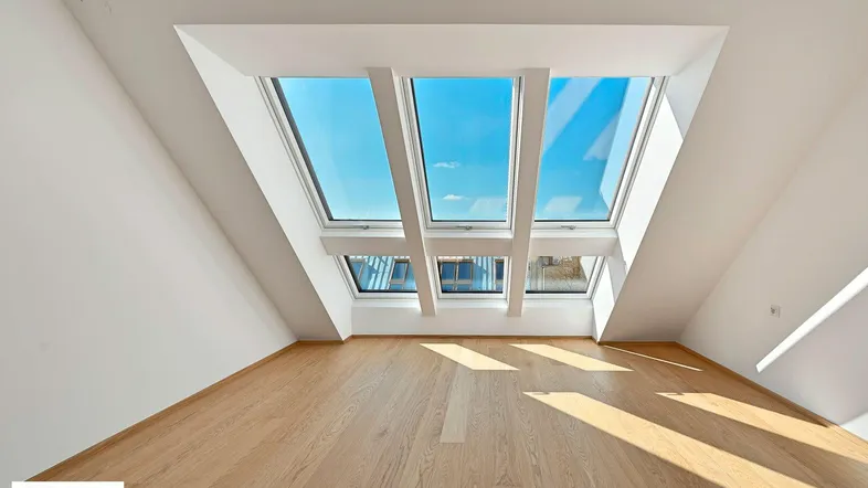 Lichtdurchfluteter Dachgeschossraum mit Holzboden und großen Dachfenstern, die viel Sonne hereinlassen.