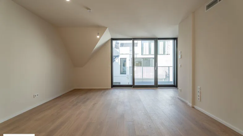 Heller Wohnraum mit Parkettboden, Dachschräge und Zugang zu einem Balkon.