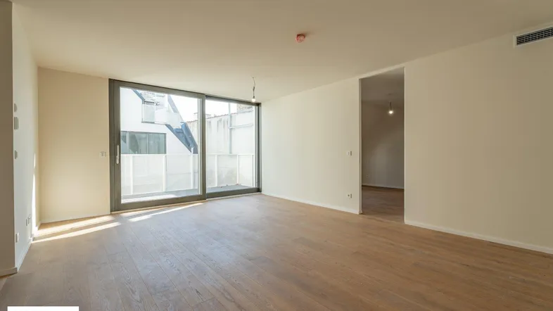 Helles, leeres Wohnzimmer mit Holzboden und großen Schiebetüren zum Außenbereich.