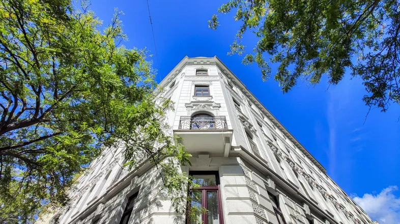 Historisches Eckgebäude mit klassischer Architektur und dekorativen Elementen unter blauem Himmel.