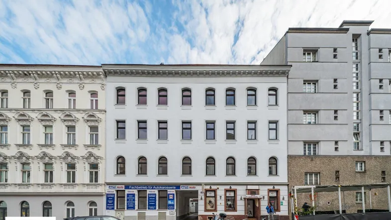 Historisches Gebäude mit klassischer Fassade und Geschäften im Erdgeschoss in einer städtischen Umgebung.