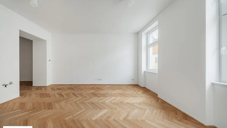 Geräumiges, helles Zimmer mit Fischgrätparkett und einem großen Fenster, ideal für Wohnzwecke.