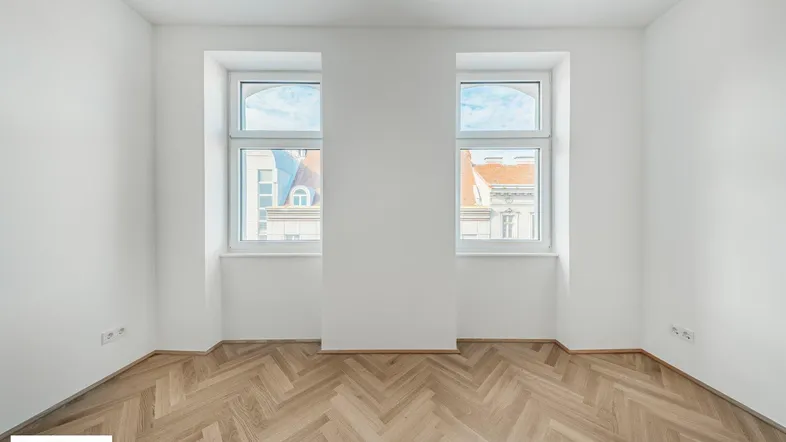 Helles Zimmer mit Fischgrätparkett und weißen Wänden, bietet einen Blick auf die umliegenden Gebäude.