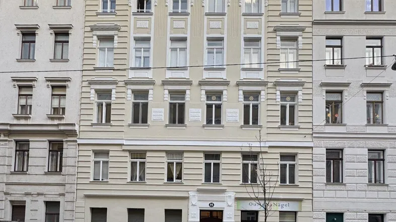 Historisches Gebäude mit reich verzierter Fassade und klassischen Fenstern an einer städtischen Straße.