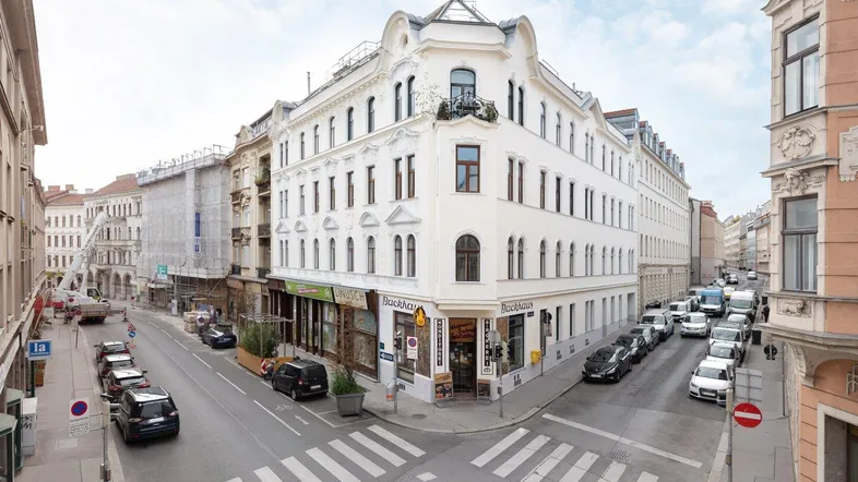 Historisches Eckgebäude in urbaner Umgebung mit klassischer Architektur und belebten Straßenansichten.