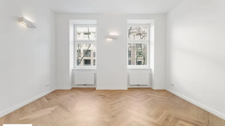 Helles Zimmer mit Fischgrätparkett und zwei großen Fenstern, ideal als Wohn- oder Schlafzimmer.