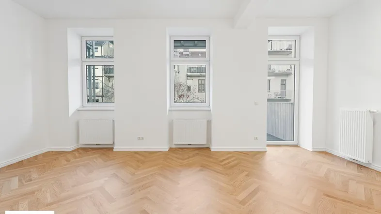 Helles Wohnzimmer mit Fischgrätparkettboden, weißen Wänden und Zugang zu einem Balkon.