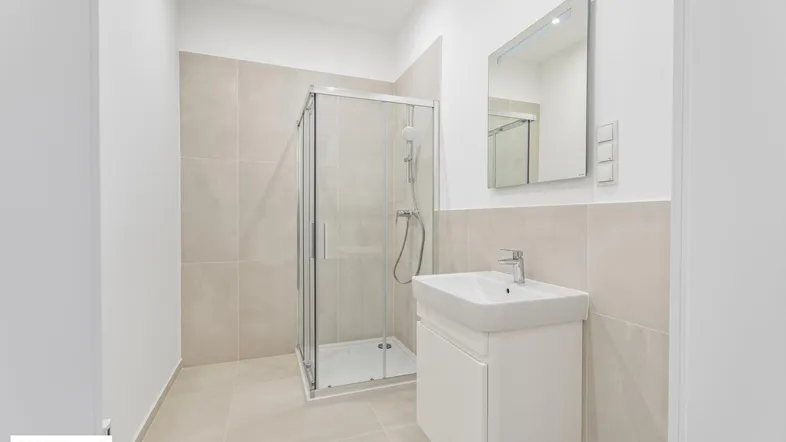 Modernes Badezimmer mit beigefarbenen Fliesen, einer Duschkabine und einem einzelnen Waschbecken.