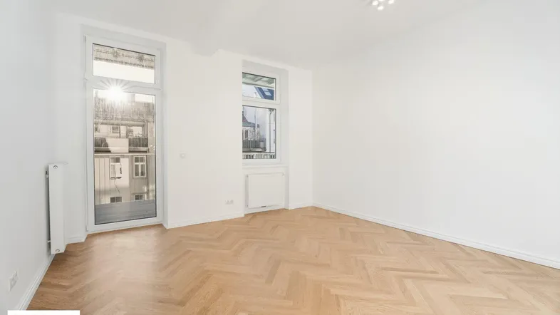 Helles, leeres Zimmer mit Fischgrätparkett und Zugang zu einem französischen Balkon.