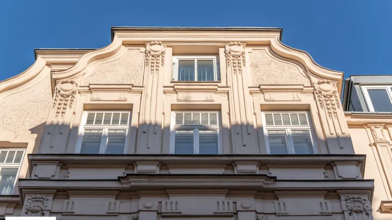 Detailansicht der reich verzierten Fassade eines Altbaus mit Mansarddach und Stuckelementen.