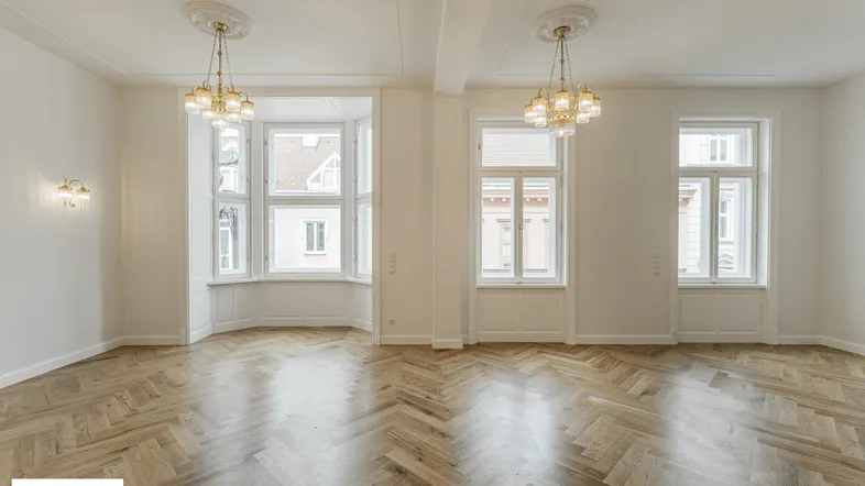Eleganter Wohnraum mit Erkerfenstern, Fischgrätparkett und klassischen Deckenleuchten.