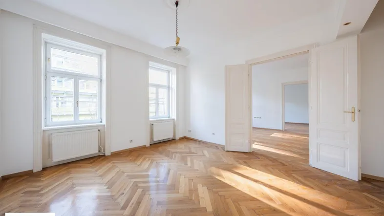 Helles Wohnzimmer mit Fischgrätparkett und hohen Doppeltüren zu weiteren Räumen.
