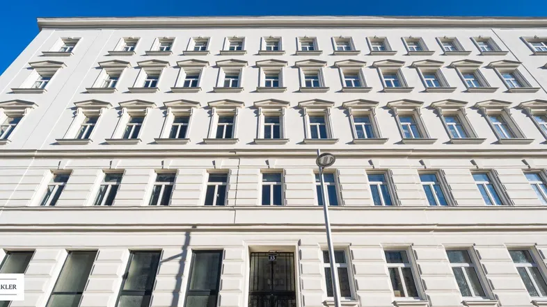 Klassische weiße Fassade eines Altbaus mit vielen Fenstern unter blauem Himmel.