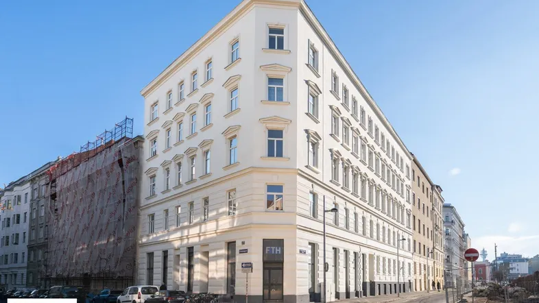 Eckgebäude mit klassischer Architektur und vielen Fenstern in urbaner Umgebung.