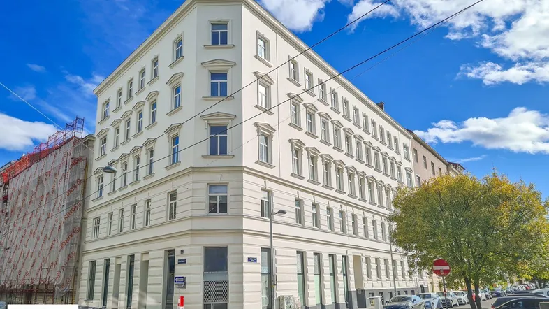 Elegantes Eckgebäude mit klassischer Architektur und vielen Fenstern, umgeben von städtischer Umgebung.