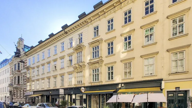 Historisches Gebäude mit klassischer Fassade und Geschäften im Erdgeschoss, geparkt an einer belebten Straße.