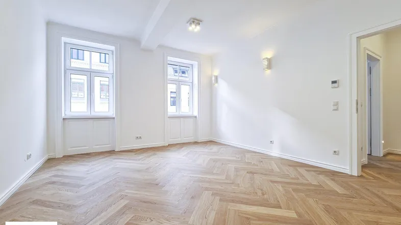 Helles Zimmer mit Fischgrätparkett und hohen Fenstern, bereit zur individuellen Gestaltung.