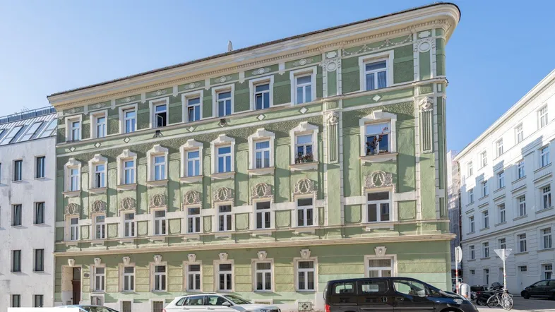 Historisches Eckgebäude mit grüner Fassade und vielen Fenstern in städtischer Umgebung.