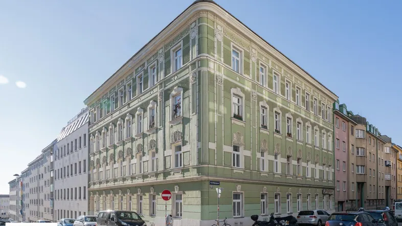 Historisches Eckgebäude mit hellgrüner Fassade und eleganten Stuckverzierungen an einer städtischen Straße.